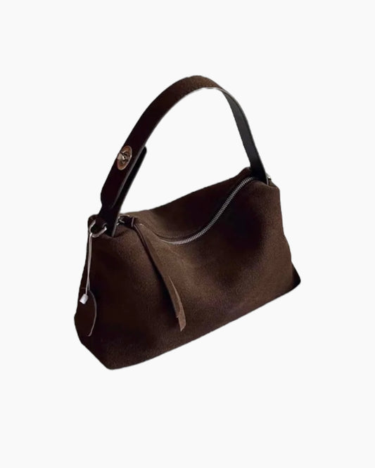 Evelyn Taske i mørkebrunt ruskind med kort skulderrem og sølvfarvet metaldetalje. Elegant hobo-design med aftagelig lang crossbody-rem og diskret lynlaaslukning. Tidløs hverdagstaske i blød kvalitet.